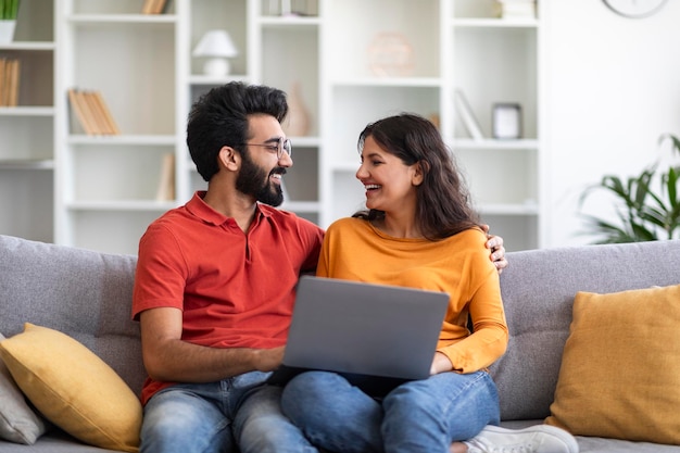 Retrato de una pareja india feliz con una computadora portátil relajándose en el sofá en casa