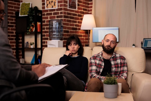 Retrato de una pareja infeliz hablando con un consejero en una sesión de terapia, tratando de resolver las dificultades de la relación junto con el terapeuta. Lidiando con problemas matrimoniales en el apoyo de consejería.