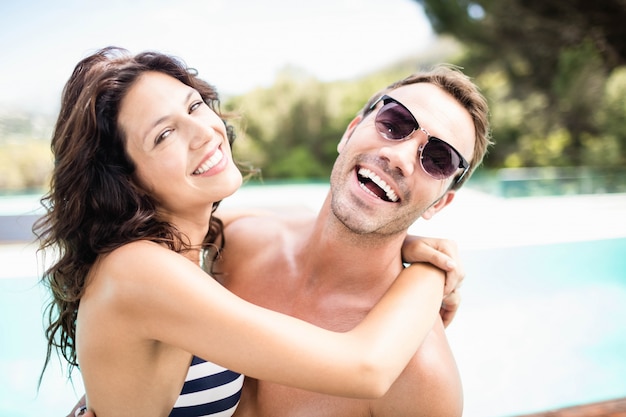 Retrato de una pareja joven abrazándose unos a otros cerca de la piscina en un día soleado