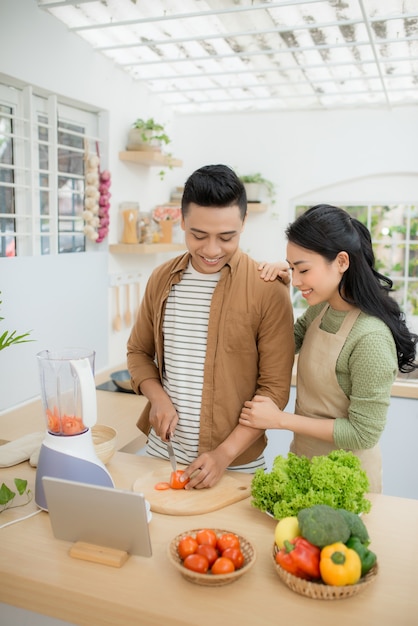 Retrato de una pareja joven y bonita cocinando juntos según una receta en una tableta