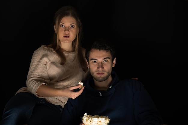 Foto retrato de una pareja joven comiendo palomitas de maíz mientras está sentada contra un fondo negro