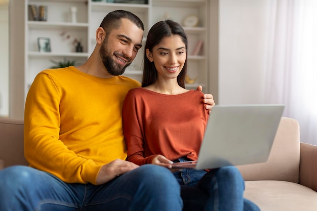 Retrato de una pareja joven y feliz navegando por Internet en una computadora portátil en casa