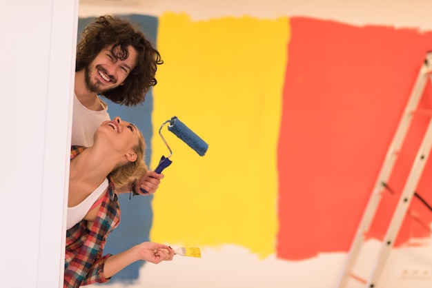 retrato de una pareja joven feliz y sonriente pintando la pared interior de una casa nueva asomándose desde detrás de la pared