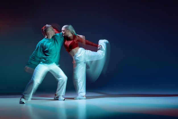 Retrato de pareja joven hombre y mujer bailando danza de estilo moderno aislado sobre fondo azul oscuro