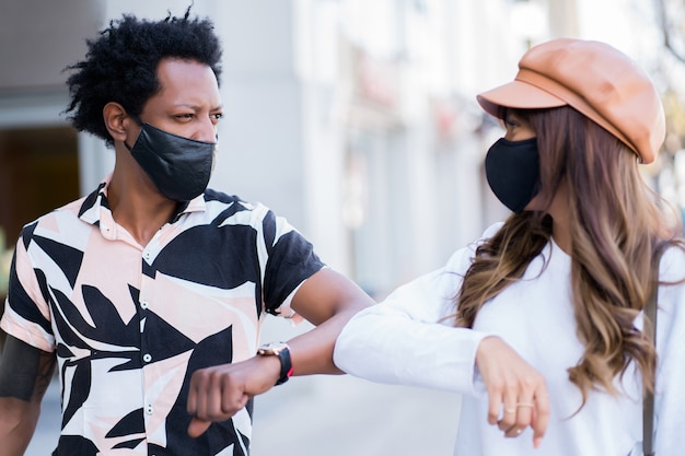 Retrato de pareja joven con mascarilla y tocándose con los codos para saludar mientras está de pie al aire libre