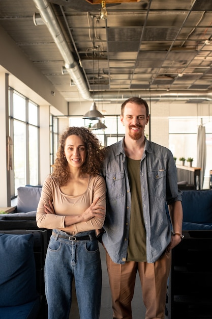 Retrato de pareja joven positiva de propietarios de cafés parados juntos en establecimiento loft