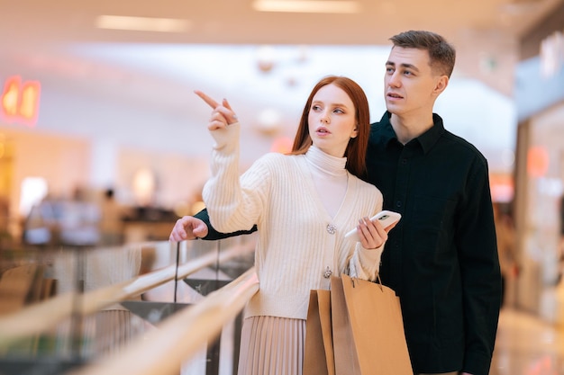 Retrato de pareja joven con problemas en busca de tienda en el centro comercial aplicación de navegación en el móvil