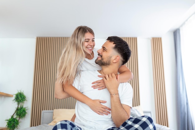 Retrato de una pareja joven sentada en la cama y mirándose Atractivo y hermoso nuevo matrimonio hombre y mujer en pijama disfrutan de la actividad matutina en el dormitorio en casa Concepto de relación familiar