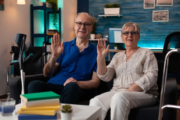 Retrato de pareja de jubilación sentada en el sofá agitando las manos