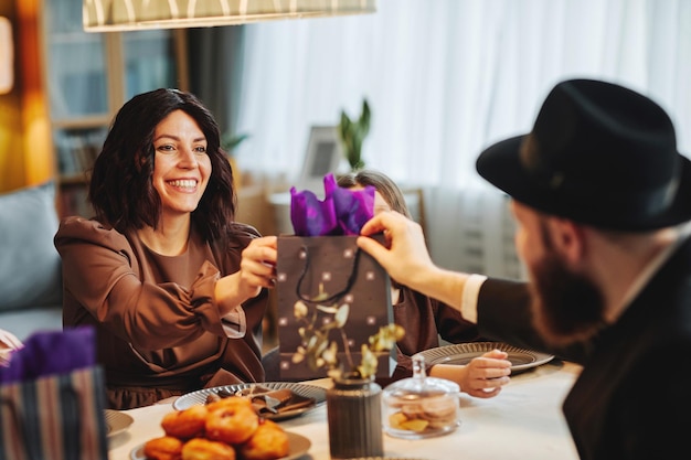 Retrato de una pareja judía adulta compartiendo regalos en la mesa de la cena en un hogar acogedor