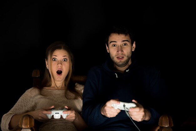 Foto retrato de una pareja jugando a un videojuego contra un fondo negro