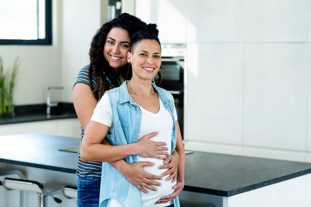 Retrato de una pareja de lesbianas embarazadas abrazando en la cocina