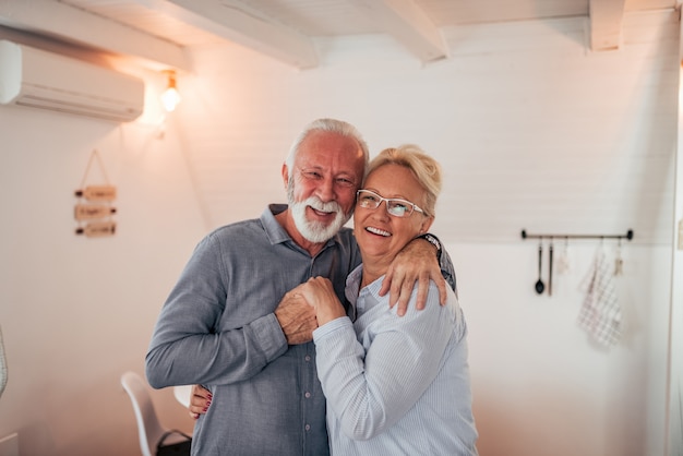 Foto retrato de una pareja mayor amorosa en el interior. abrazando, sonriendo y mirando a cámara.