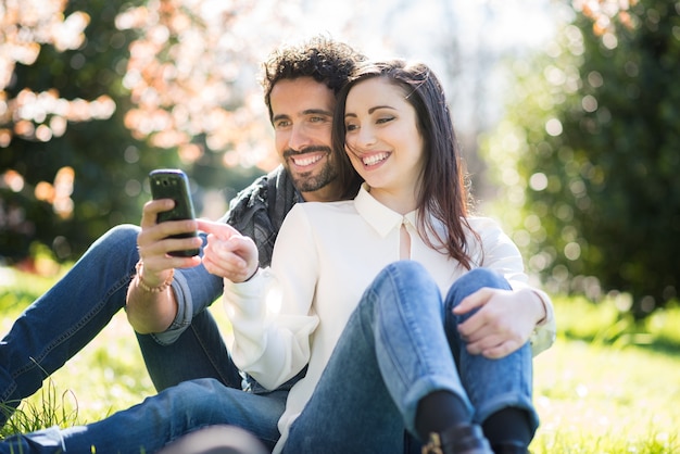 Retrato de una pareja mirando a un teléfono inteligente en un parque