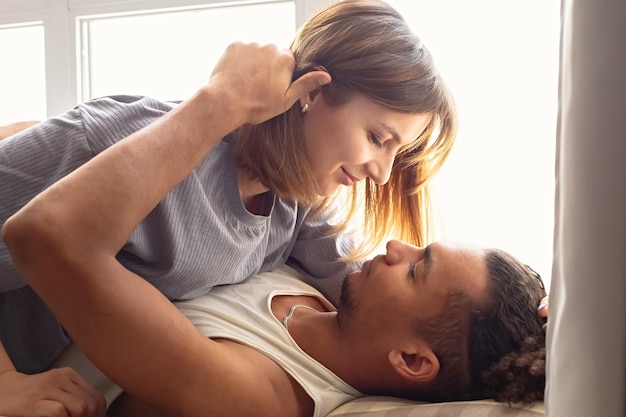 Retrato de una pareja multirracial novio y novia cara a cara yacen cerca de la ventana