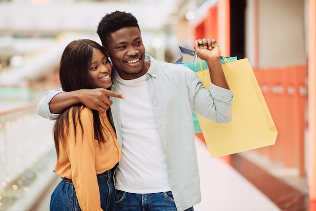 retrato, de, pareja negra, con, bolsas de compras, señalar, en, ventana