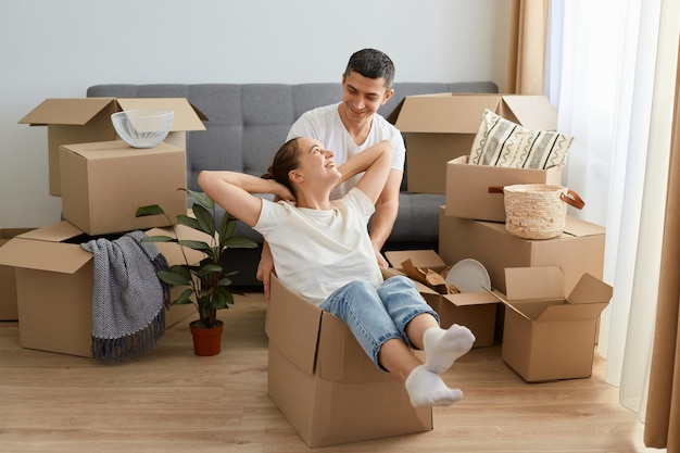 Retrato de una pareja optimista divirtiéndose con cajas de cartón en un piso nuevo el día de la mudanza esposa y esposo regocijándose por mudarse a un nuevo departamento expresando amor y gentileza