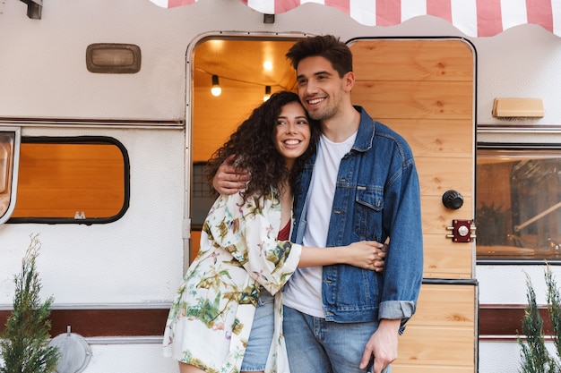 Retrato de pareja romántica hombre y mujer sonriendo mientras se abrazan cerca de la casa sobre ruedas al aire libre