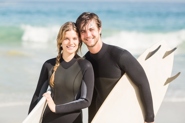Retrato de pareja con tabla de surf de pie en la playa