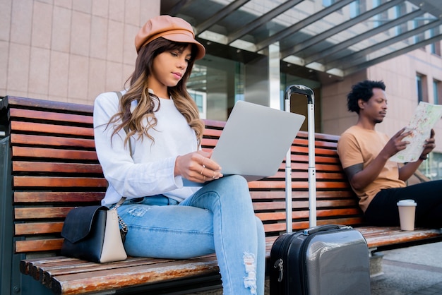 Retrato de una pareja de turistas sentados en un banco fuera del aeropuerto o de la estación de tren