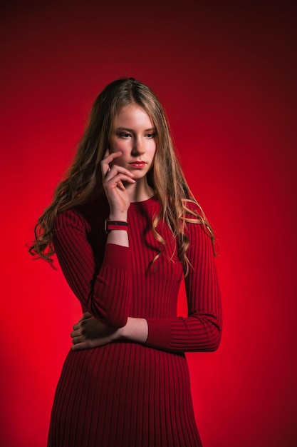 Retrato pensando jovencita cerrada elegante vestido rojo sobre fondo rojo.