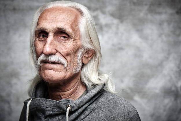 Retrato de un pensionista caucásico de pelo gris envejecido. Genial abuelo con bigote y cara sonriente mirando a la cámara sobre fondo gris con espacio de copia