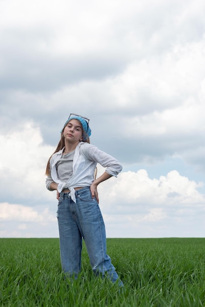 Retrato de una pequeña adolescente en un campo de hierba verde contra el telón de fondo de un cielo nublado