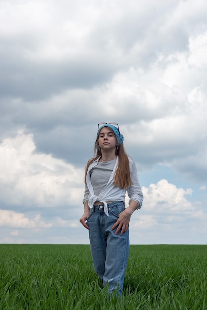 Retrato de una pequeña adolescente en un campo de hierba verde, con el telón de fondo de un cielo nublado