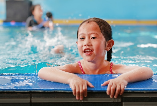 Retrato de la pequeña muchacha asiática feliz del niño que aprende nadar en piscina. Primer plano corto.