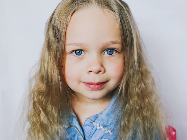 Retrato de una pequeña niña hermosa de ojos azules, sobre fondo blanco.