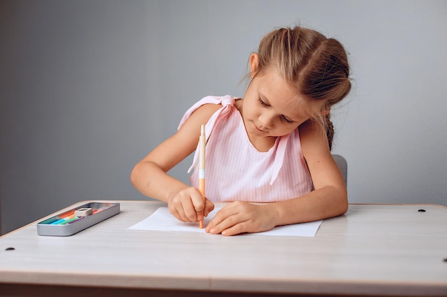 Retrato de una pequeña niña ordenada diligente sentada en una mesa y dibujo en papel con crayones. Concepto de infancia. foto con ruido