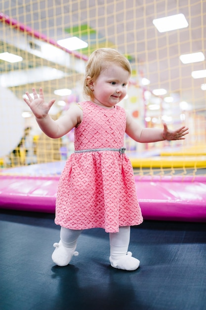 Retrato pequeno bebê fofo criança menina princesa infantil 1-2 anos brincando e pulando em uma cama elástica na sala de jogos infantil, interior na festa de aniversário. Férias de conceito de celebração, evento, entretenimento.