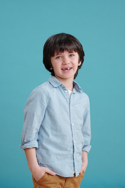 Retrato de pequeño colegial en camiseta sonriendo a la cámara contra el fondo azul.