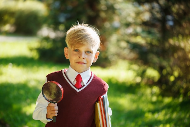 Retrato pequeño colegial en la naturaleza. Niño con libros y lupa. Educación para niños. Concepto de regreso a la escuela