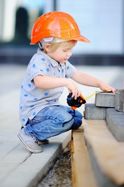 Foto retrato del pequeño constructor lindo en cascos con la regla que trabaja al aire libre