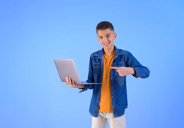 Retrato de un pequeño hombre de negocios sonriendo y señalando a la computadora portátil mientras trabaja en un fondo azul aislado