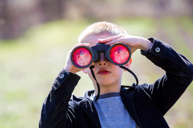 Retrato de pequeño lindo chico guapo lindo rubio mirando atentamente algo a través de binoculares