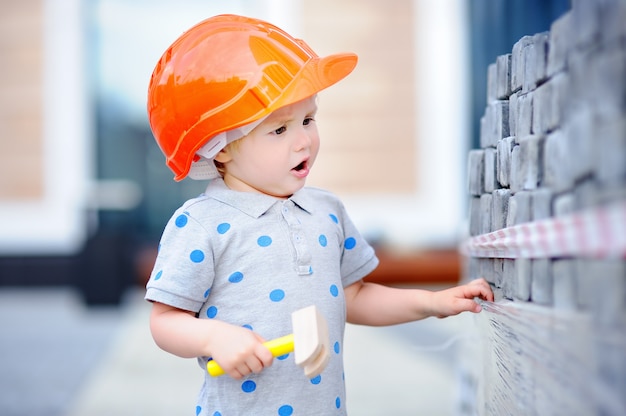 Retrato del pequeño y lindo constructor en cascos con martillo trabajando al aire libre