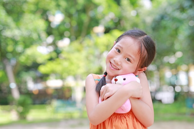 Retrato del pequeño niño asiático feliz en jardín verde con el abrazo del oso de peluche y mirando a la cámara.