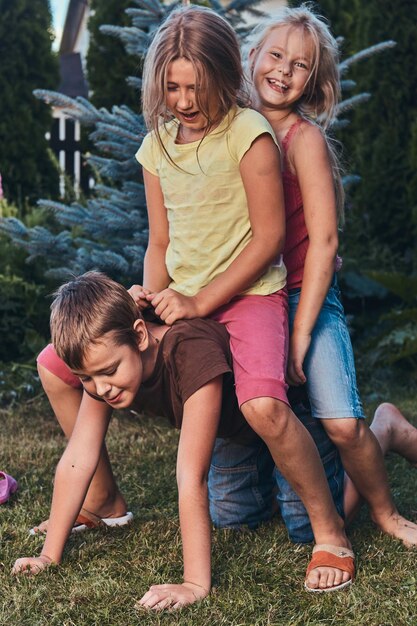 Retrato de pequeños amigos felices divirtiéndose en el patio. Niño sosteniendo a dos niñas en la espalda.