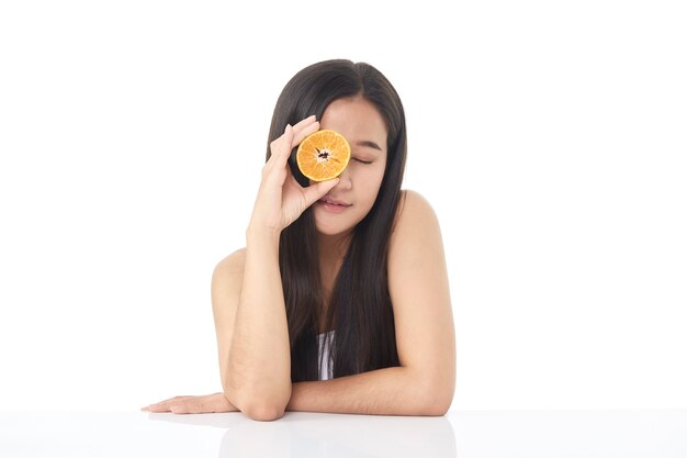 Retrato perfeito da pele fresca da bela jovem asiática com fatias de laranja na mão, isoladas no fundo branco