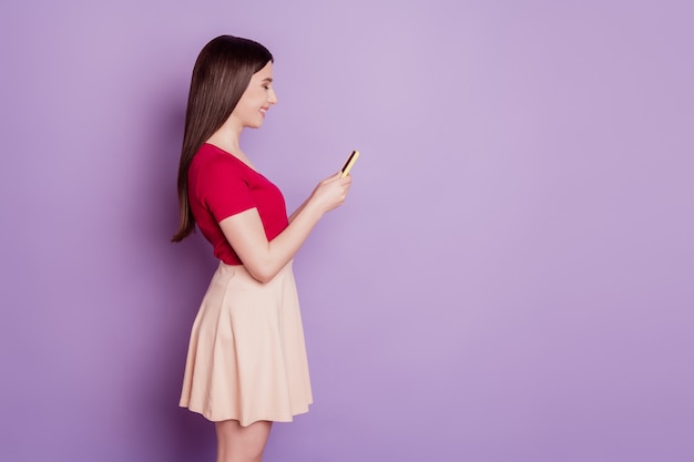 Retrato de perfil de dama encantadora alegre mantenga la pantalla de aspecto de mensajes de texto de teléfono móvil sobre fondo violeta