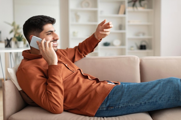 Retrato de perfil del hombre hablando por teléfono celular sentado en el sofá