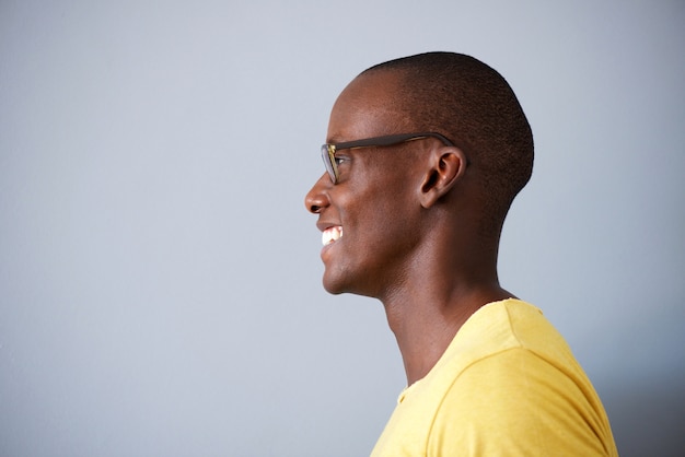 Retrato de perfil de hombre negro sonriendo con gafas contra el fondo gris
