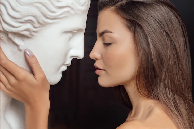 Retrato de perfil de una mujer hermosa joven de pie junto a una escultura de yeso de venus