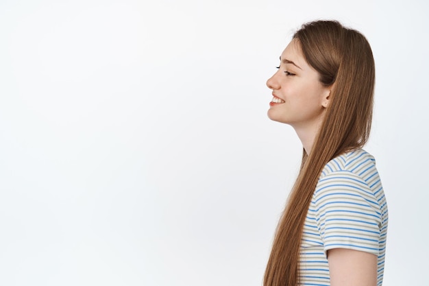 Foto retrato de perfil de mujer joven con cabello largo natural y saludable, sonriendo feliz y mirando a la izquierda en el espacio vacío, fondo blanco