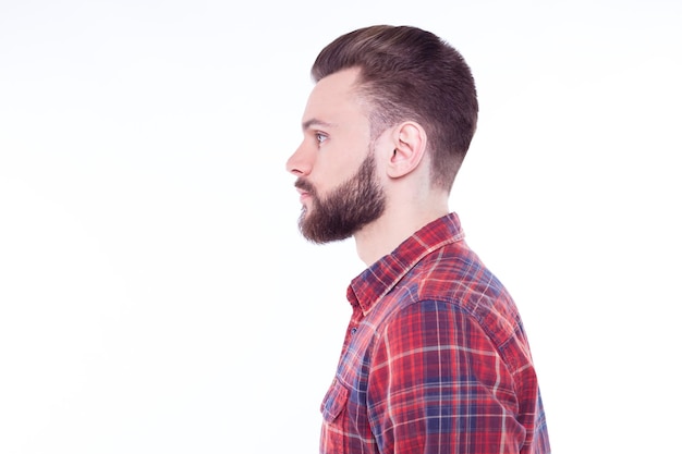 Retrato de perfil o vista lateral de un apuesto joven barbudo con estilo en camisa a cuadros aislado sobre fondo blanco