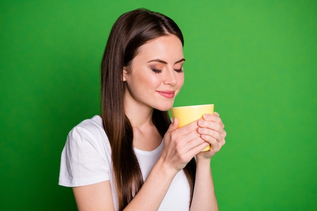 Retrato de perfil de la tranquila dama morena agradable beber cacao cerrar los ojos visten camiseta blanca aislada sobre fondo de color verde