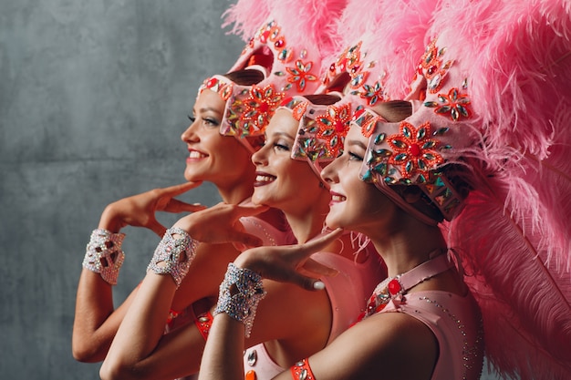 Retrato de perfil de tres mujeres en traje de samba o lambada con plumaje de plumas rosas