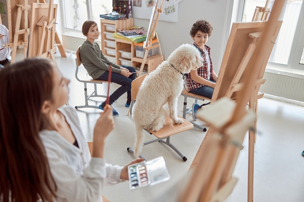 Retrato de un perro estudiante en una lección de dibujo grupal en un aula de luz moderna